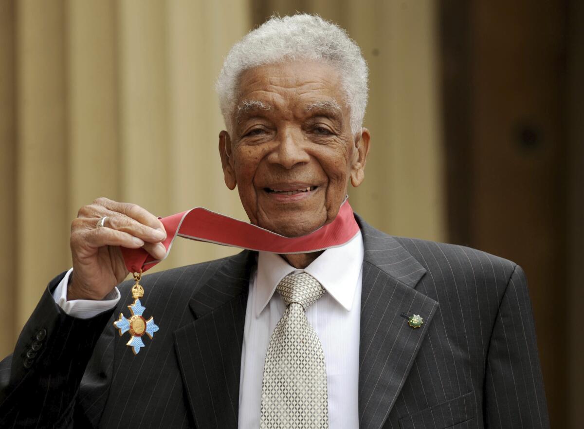 Earl Cameron poses for the media outside Buckingham Palace after being presented his CBE by Prince Charles, in London. 