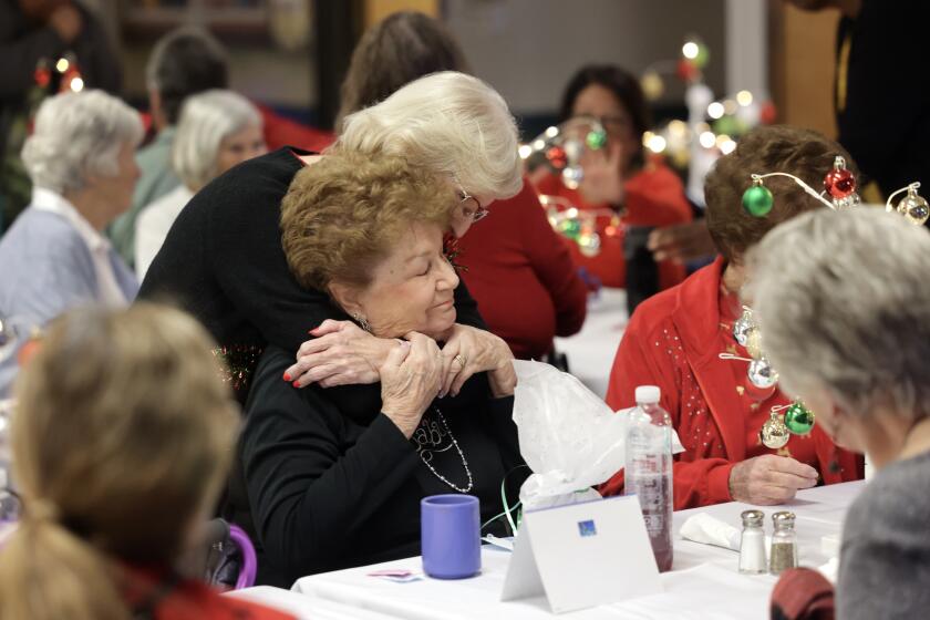 SAN MARCOS, CA - DECEMBER 21, 2023: Deanna Smith, sitting, is hugged by longtime friend Donna Read, both met at the Senior Center, during the San Marcos Senior Center's Holiday Gala in San Marcos on Thursday, December 21, 2023. (Hayne Palmour IV / For The San Diego Union-Tribune)