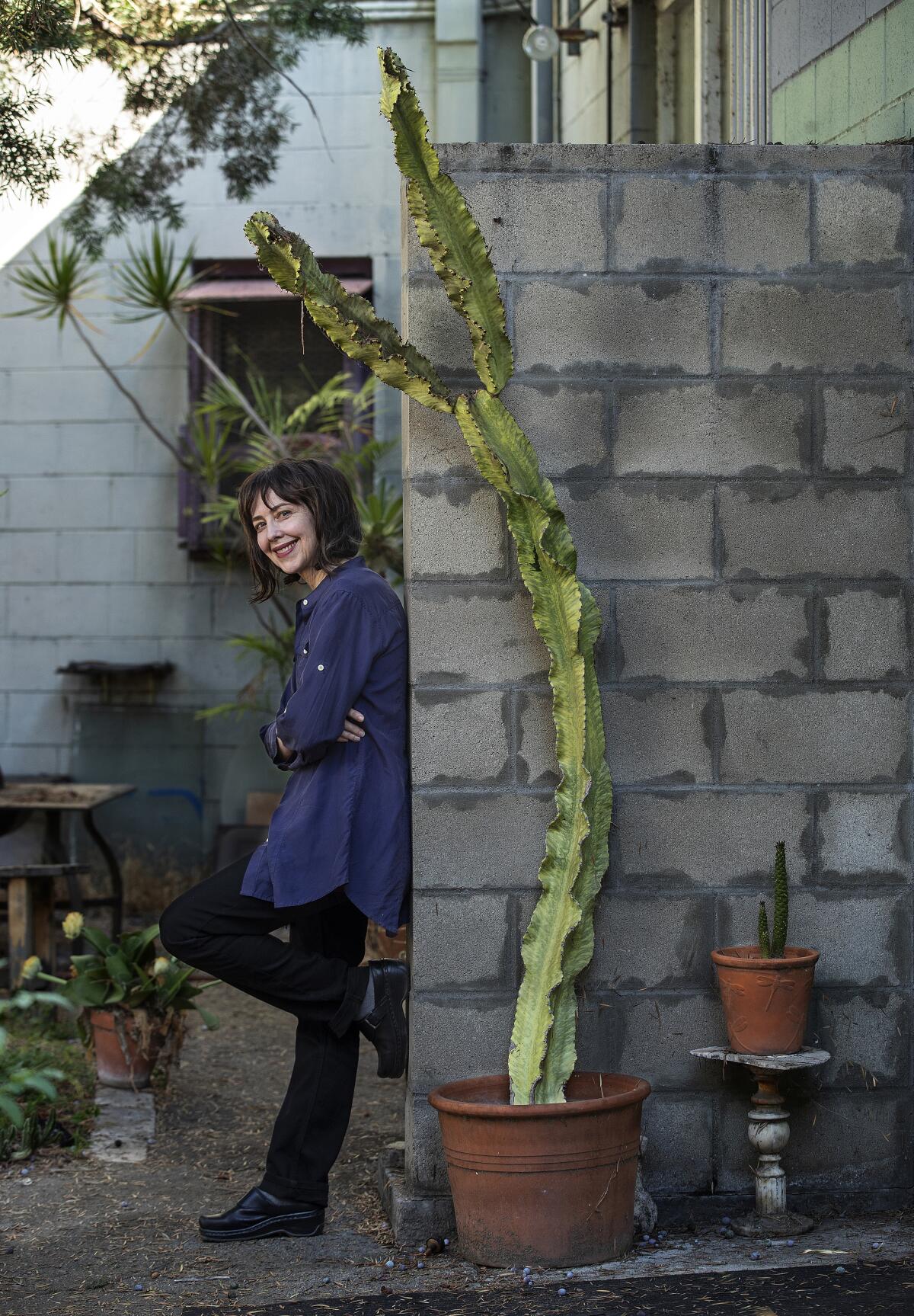 Painter Linda Stark, framed by cactus, leans against a cinderblock wall in her garden.