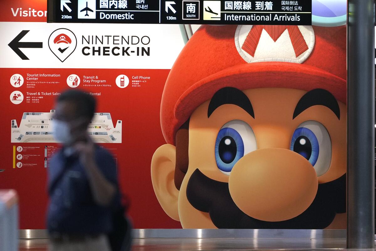 A traveler walks past an advertisement featuring a Nintendo character at Narita airport in Narita near Tokyo Friday, June 10, 2022. Nintendo reported Wednesday, Aug. 3, 2022, that its profit for the April-June quarter rose 28% from last year on healthy demand for its games, although console sales were dented by a shortage of semiconductors. (AP Photo/Shuji Kajiyama)
