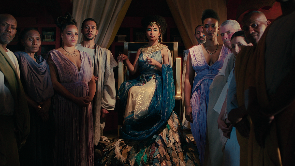 An actor portraying Cleopatra, surrounded by her court, in a new production.