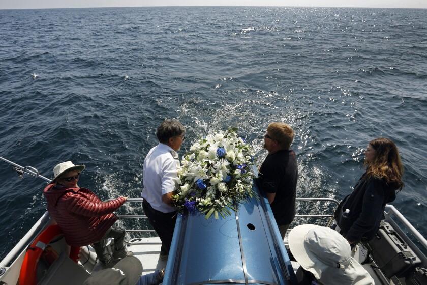 Los Angeles, California-April 1, 2022-Diane Berol, far left, stands by as the casket of her husband John Berol is buried at sea. "As a professional boat captain who has sailed around the world, I'm a semi-radical environmentalist," said his wife, Diane Berol. "I said to John, 'When we die we have to do the most ecological disposal of our bodies as possible.'" "We wanted to make the best decision for the future of life on the planet." (Carolyn Cole / Los Angeles Times)