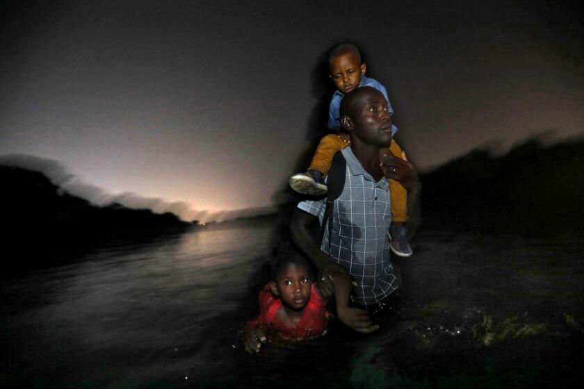 RIO GRANDE RIVER, U.S-MEXICO BORDER--JUNE 24, 2019--A Haitian man carries one child on his shoulders and drags another by his arm as he wades across the Rio Grande River, the U.S.-Mexico border, to Del Rio, Texas on Monday, June 24, 2018. (Carolyn Cole/Los Angeles Times)