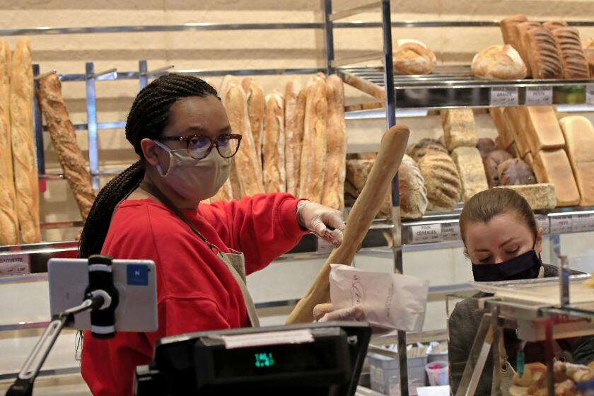 A vendor wearing a protective mask puts a baguette in a paper bag at a bakery in Paris, Monday, March 23, 2020. For most people, the new coronavirus causes only mild or moderate symptoms, such as fever and cough. For some, especially older adults and people with existing health problems, it can cause more severe illness, including pneumonia. (AP Photo/Michel Euler)