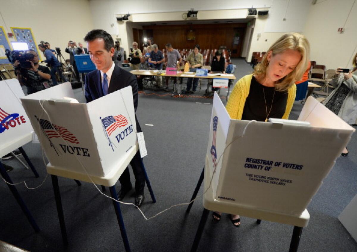 Eric Garcetti and Amy Wakeland complete their ballots inside voting booths.