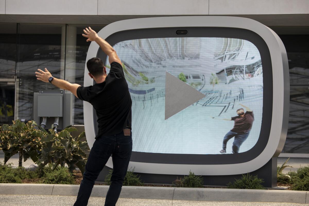 A person stretches his arms above his head and to the side in front of a giant video screen.