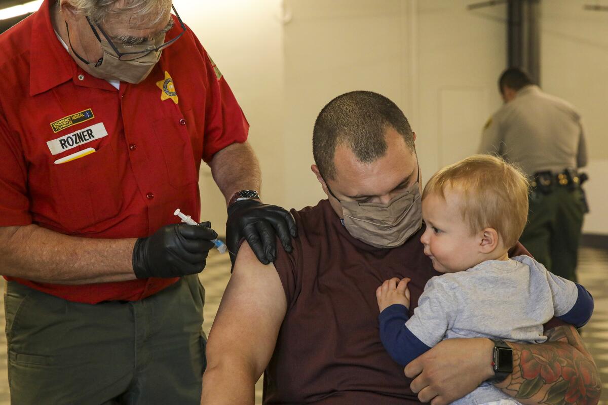 A man holding a baby receives a COVID-19 vaccination.