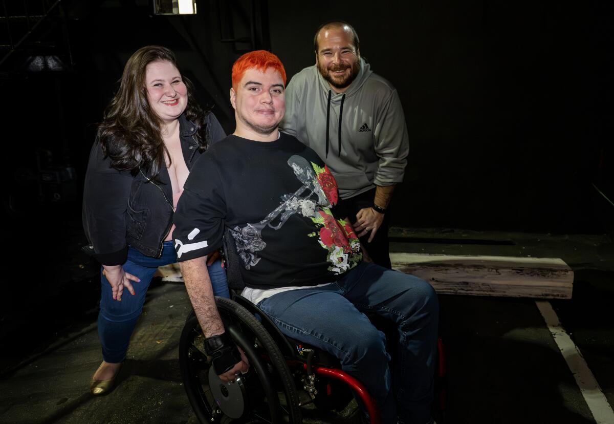 Three comedians pose together: a woman on the left, a man in a wheelchair in the middle, and another man on the right