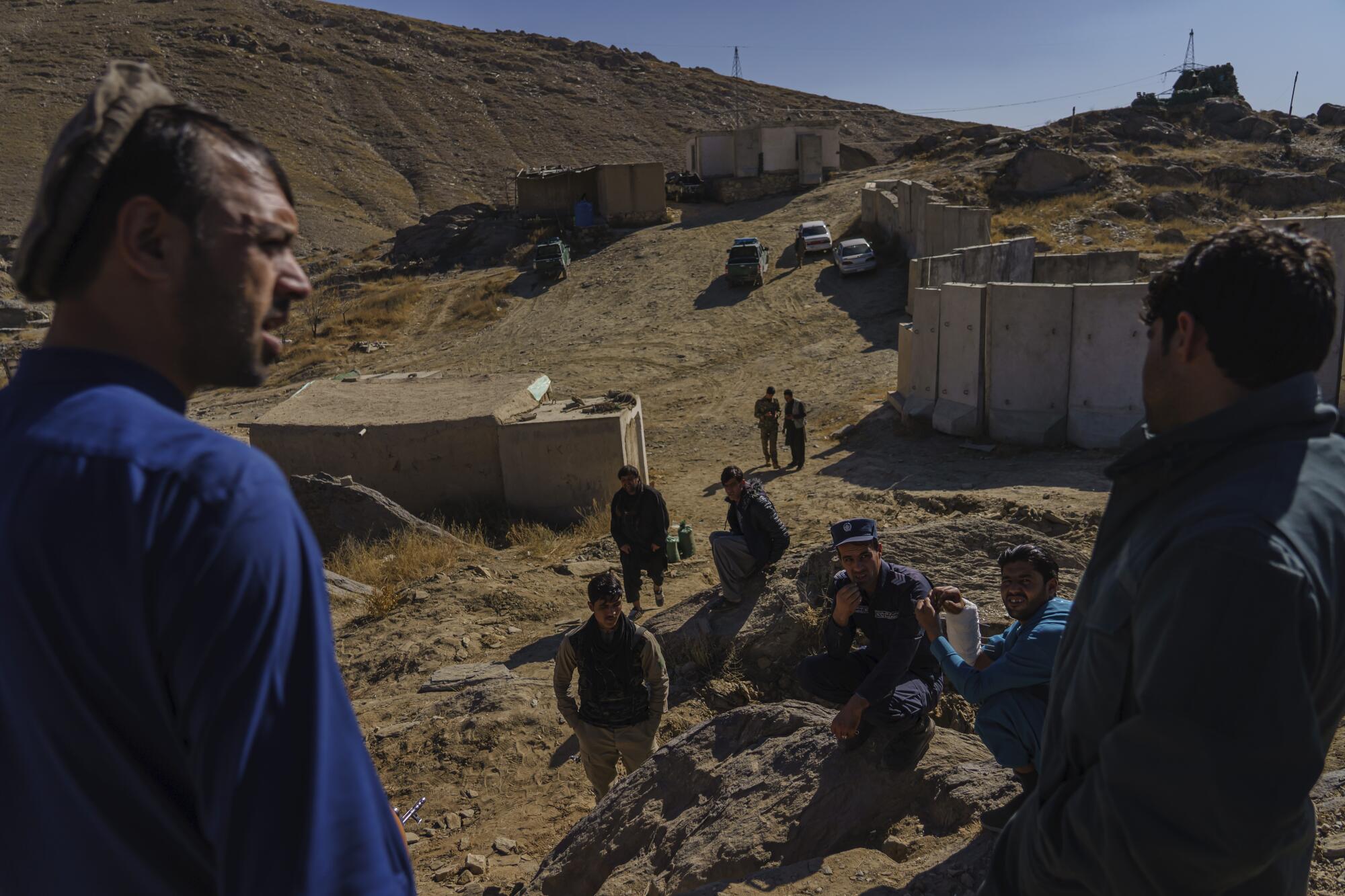 Afghan National Police commander Sarda Wali  speaks to his men, standing in an area of bare dirt hills.