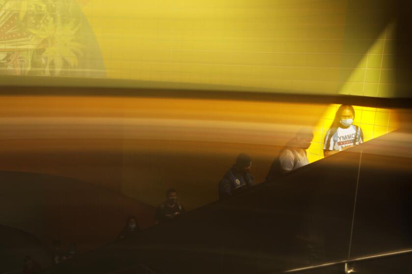 NORTH HOLLYWOOD, CA - JUNE 30, 2022 - - Commuters, caught in a reflection, make their way up an escalator after arriving at the North Hollywood Metro station in North Hollywood on June 30, 2022. The Metro board approved the $120 million five year pilot program to add 300 hundred uniformed workers on rails and buses with the aim of making riders feel safe on the system this fall. The ambassadors will be a catch-all for the system, doing everything from helping with directions to pointing people to homeless services. (Genaro Molina / Los Angeles Times)