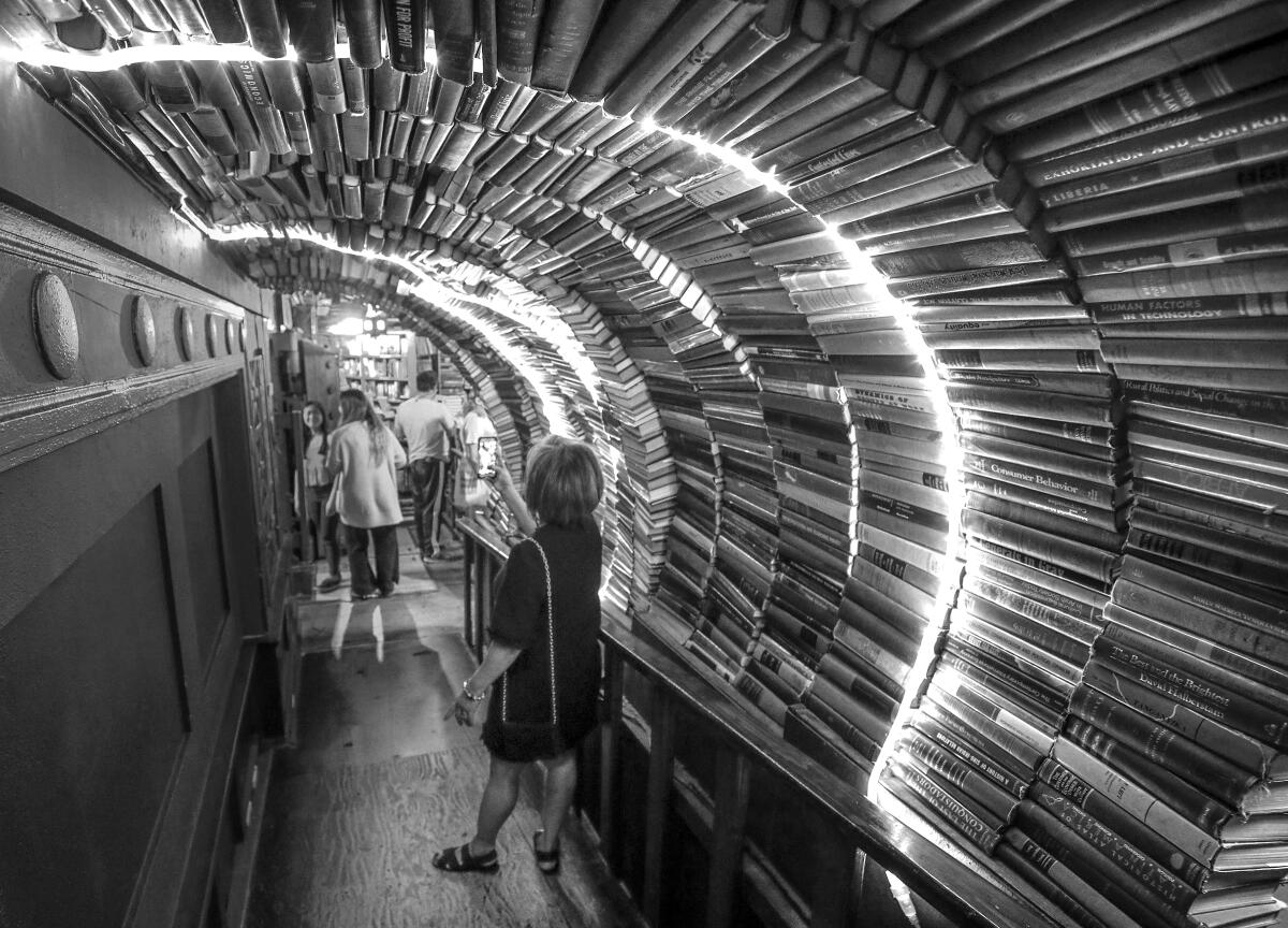 Books line a rounded passageway. A woman takes a photo with her phone.