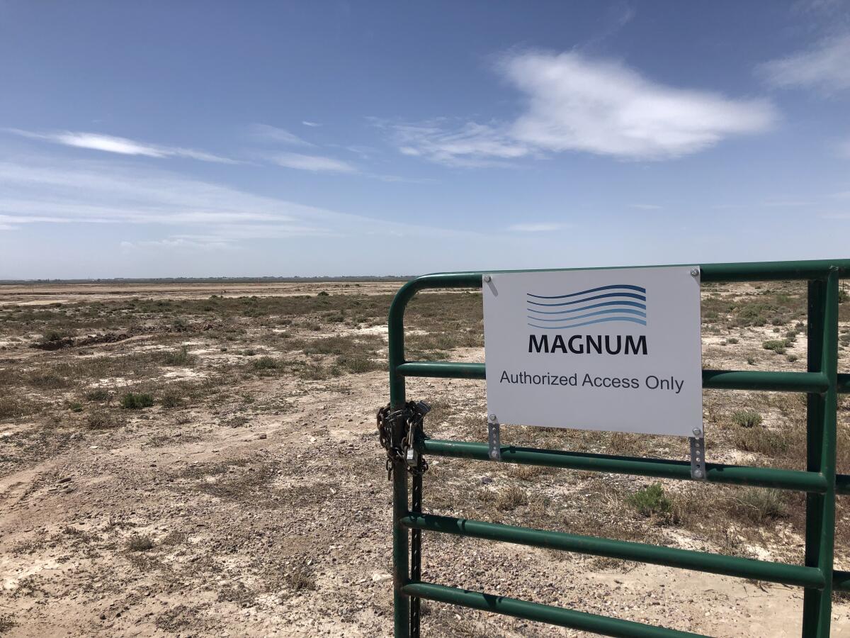 A gate has a sign that reads "Magnum, Authorized Access Only." In the background is empty landscape and blue sky.