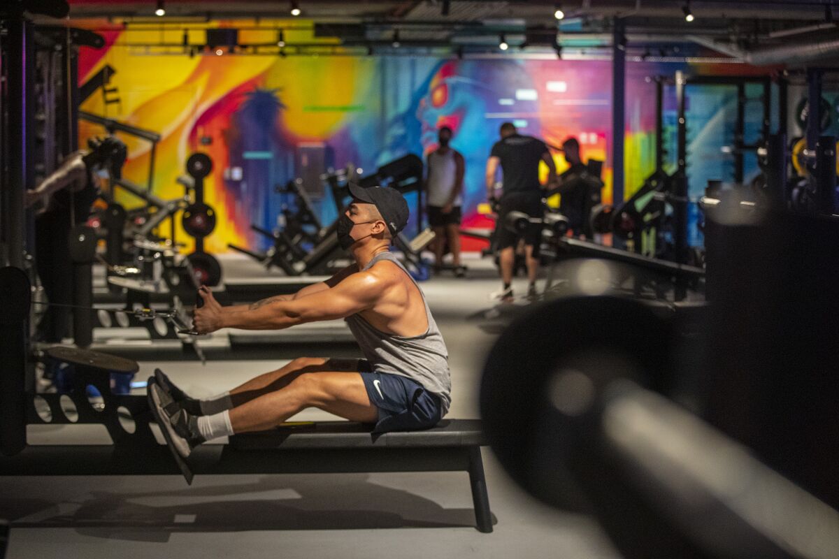A man sits and pulls on a rowing machine in a gym against a backdrop of colorful artwork