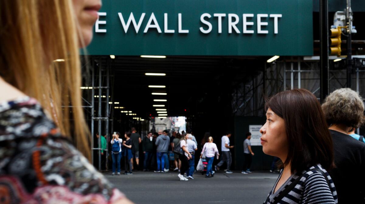 People walk past a sign for a building on Wall Street near the New York Stock Exchange.