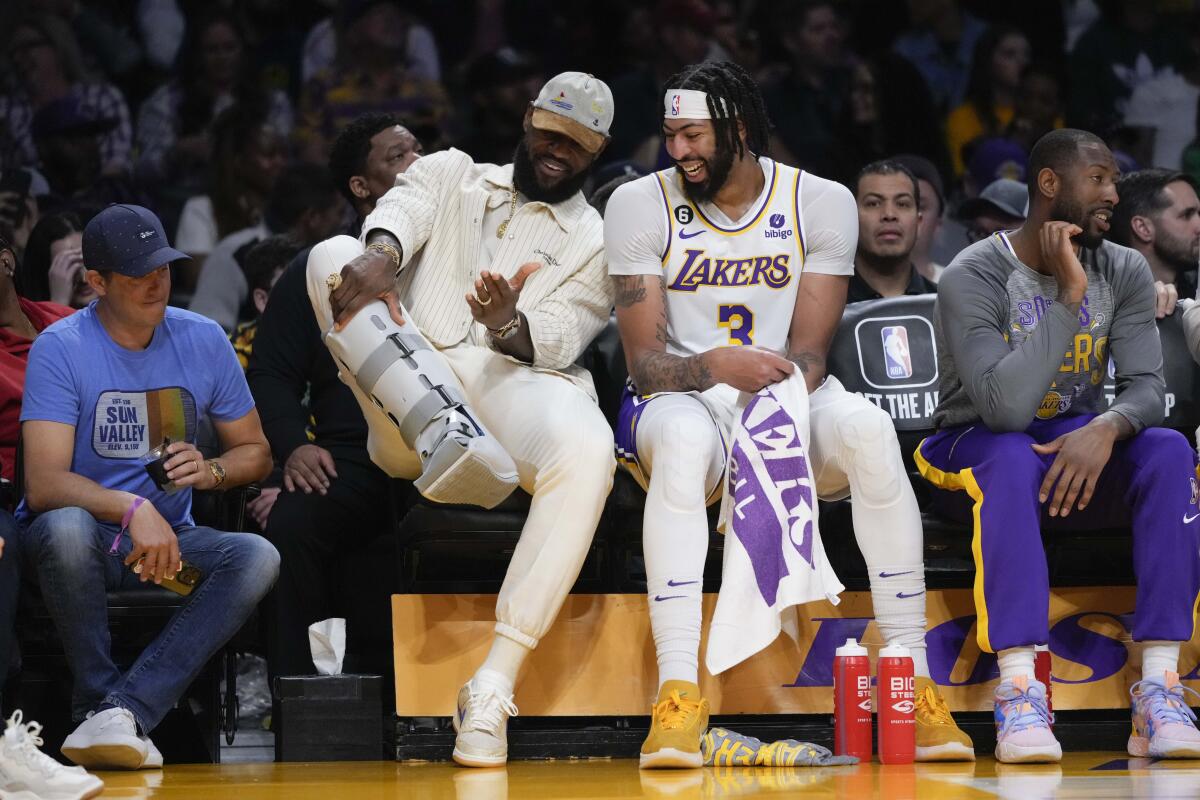 Injured Lakers star LeBron James shows teammate Anthony Davis his orthopedic boot while sitting on the bench.