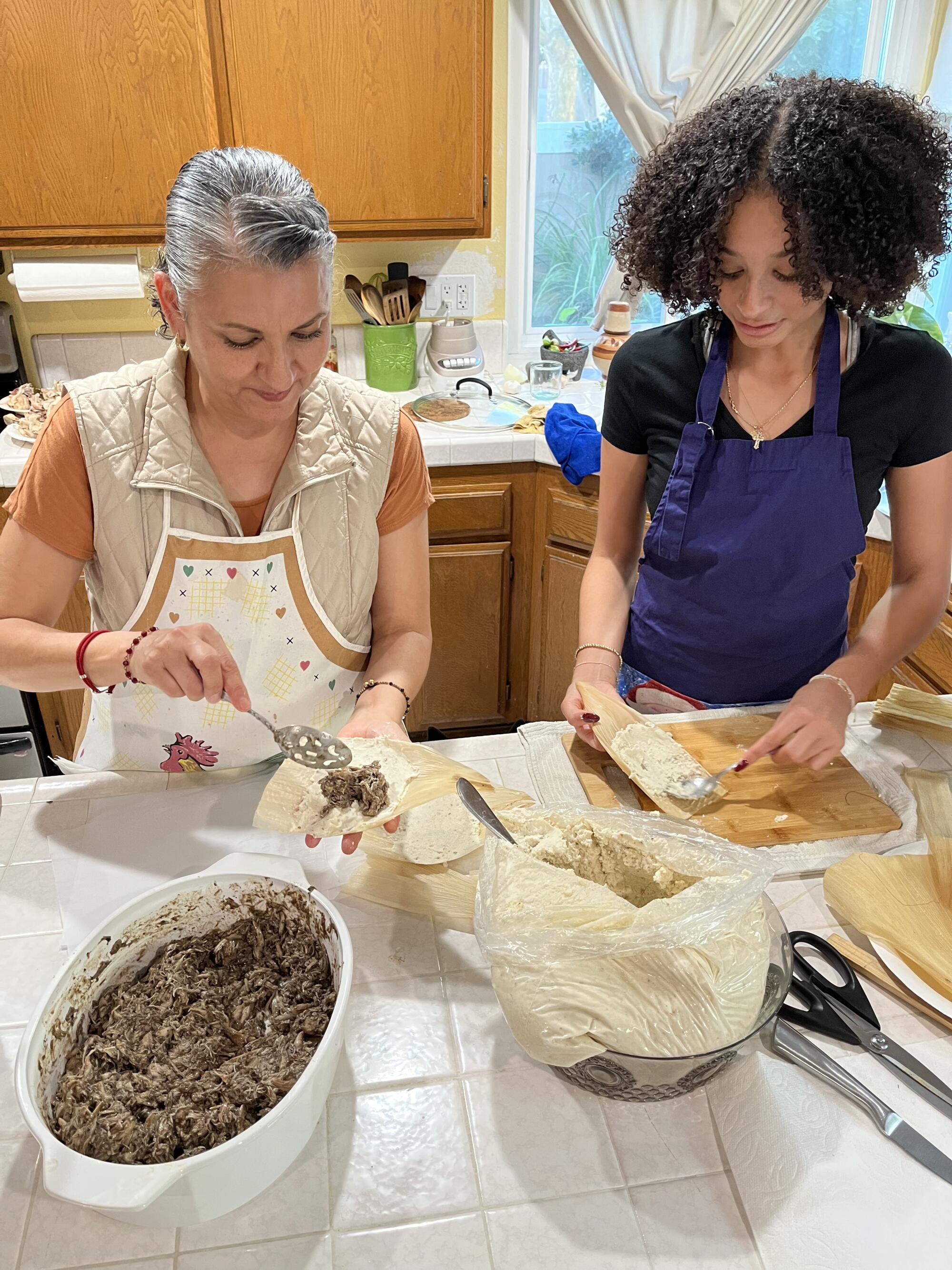 Two women in a kitchen making jerk chicken tamales