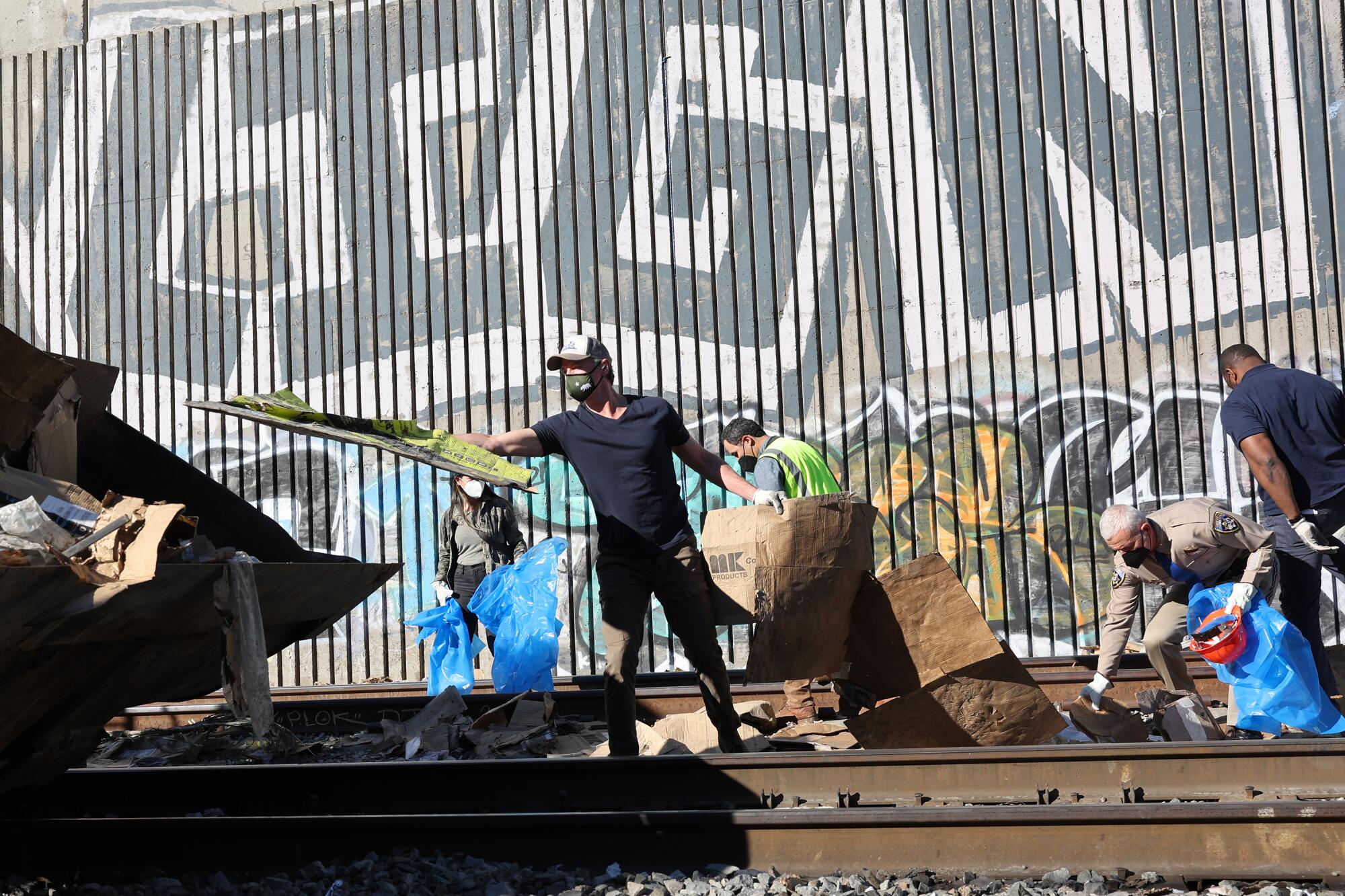Gov. Gavin Newsom helps clean debris from train tracks where cargo cars were looted in Lincoln Heights.