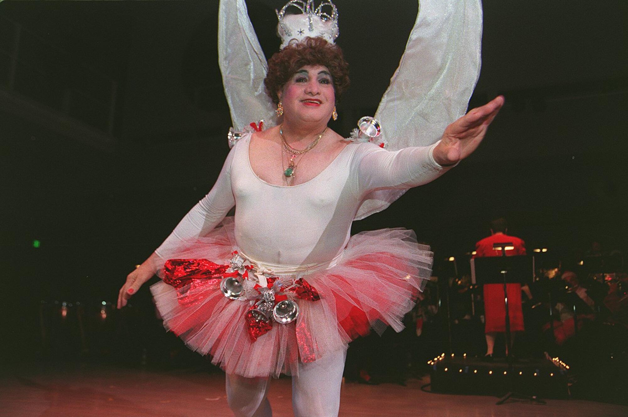 A person wears a white leotard, pink and red tutu, and crown.