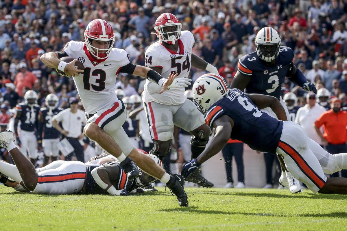Georgia quarterback Stetson Bennett (13) carries the ball as he tries to get past Auburn linebacker Zakoby McClain (9) during the first half of an NCAA college football game Saturday, Oct. 9, 2021 in Auburn, Ala. (AP Photo/Butch Dill)
