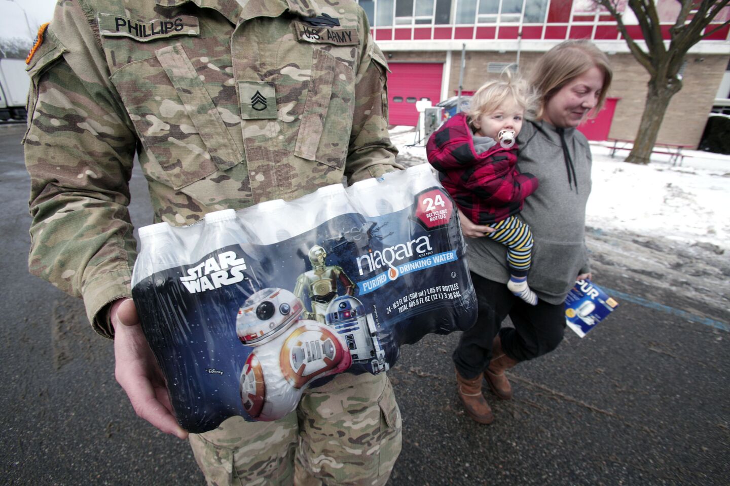 A Michigan National Guardsman helps Flint resident Amanda Roark and her son Dash unload bottled water distributed at a Flint fire station.