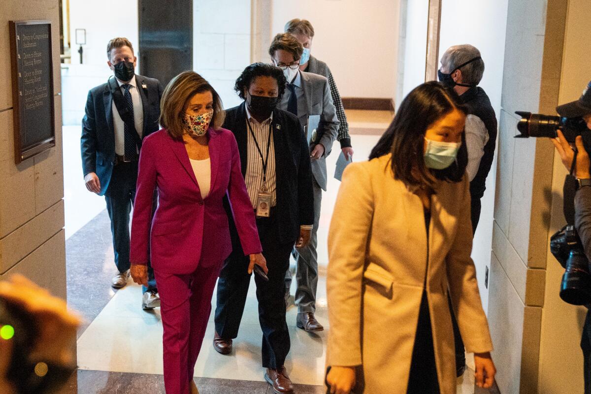Nancy Pelosi walks down a hall while other people walk near her.