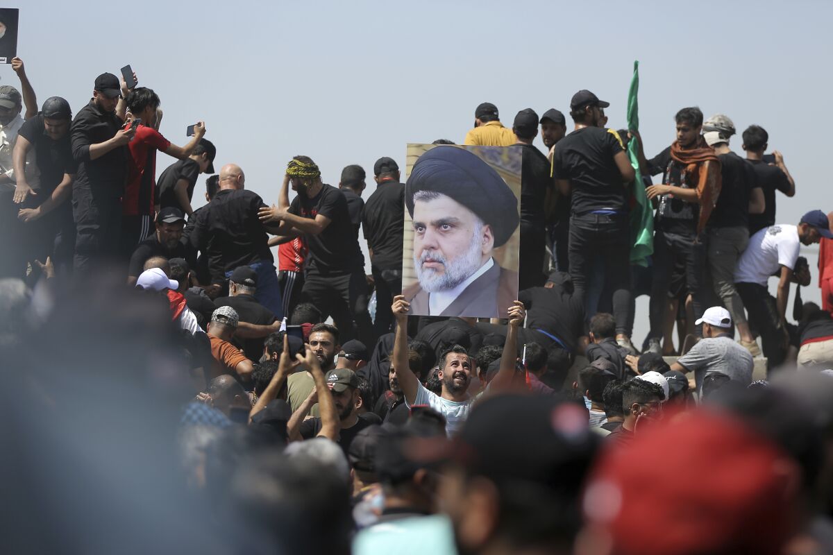 FILE - A protester holds a poster depicting Shiite cleric Muqtada al-Sadr on a bridge leading towards the Green Zone area in Baghdad, Iraq, Saturday, July 30, 2022 — days after hundreds breached Baghdad's parliament Wednesday chanting anti-Iran curses in a demonstration against a nominee for prime minister by Iran-backed parties. Iraq’s political crisis shows no signs of abating weeks after followers of an influential cleric stormed parliament. That’s despite rising public anger over a debilitating gridlock that has further weakened the country’s caretaker government and its ability to provide basic services. (AP Photo/Anmar Khalil, File)