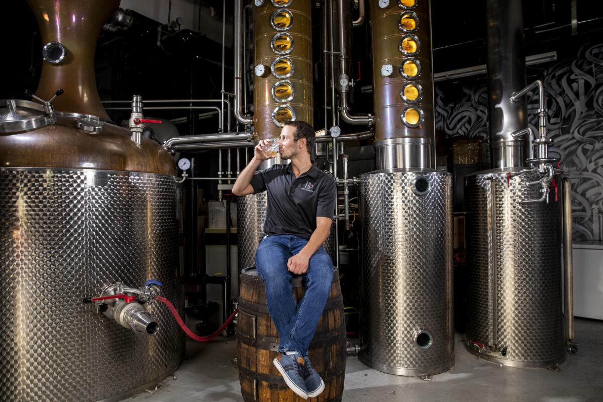 A man sits on a barrel amid distilling tanks. 