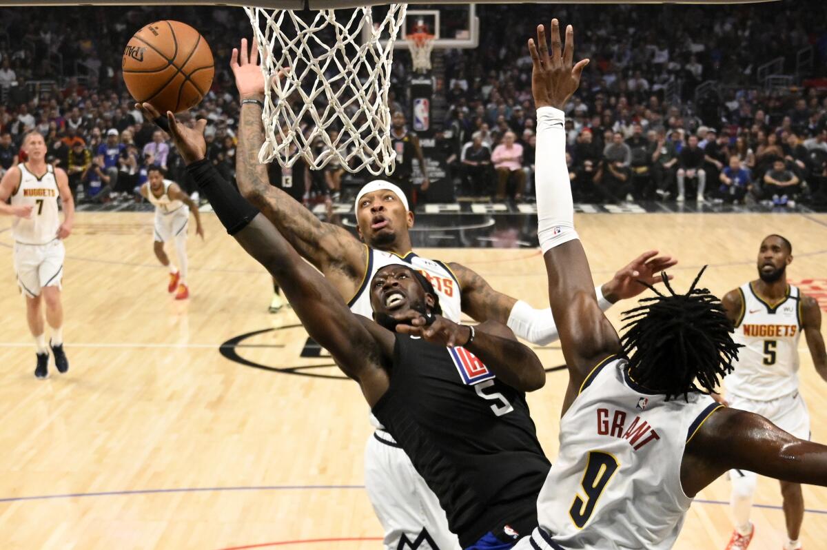 Clippers forward Montrezl Harrell (5) powers his way for a layup against Nuggets forwards Torrey Craig and Jerami Grant during the first half of a game Feb. 28, 2020, at Staples Center.