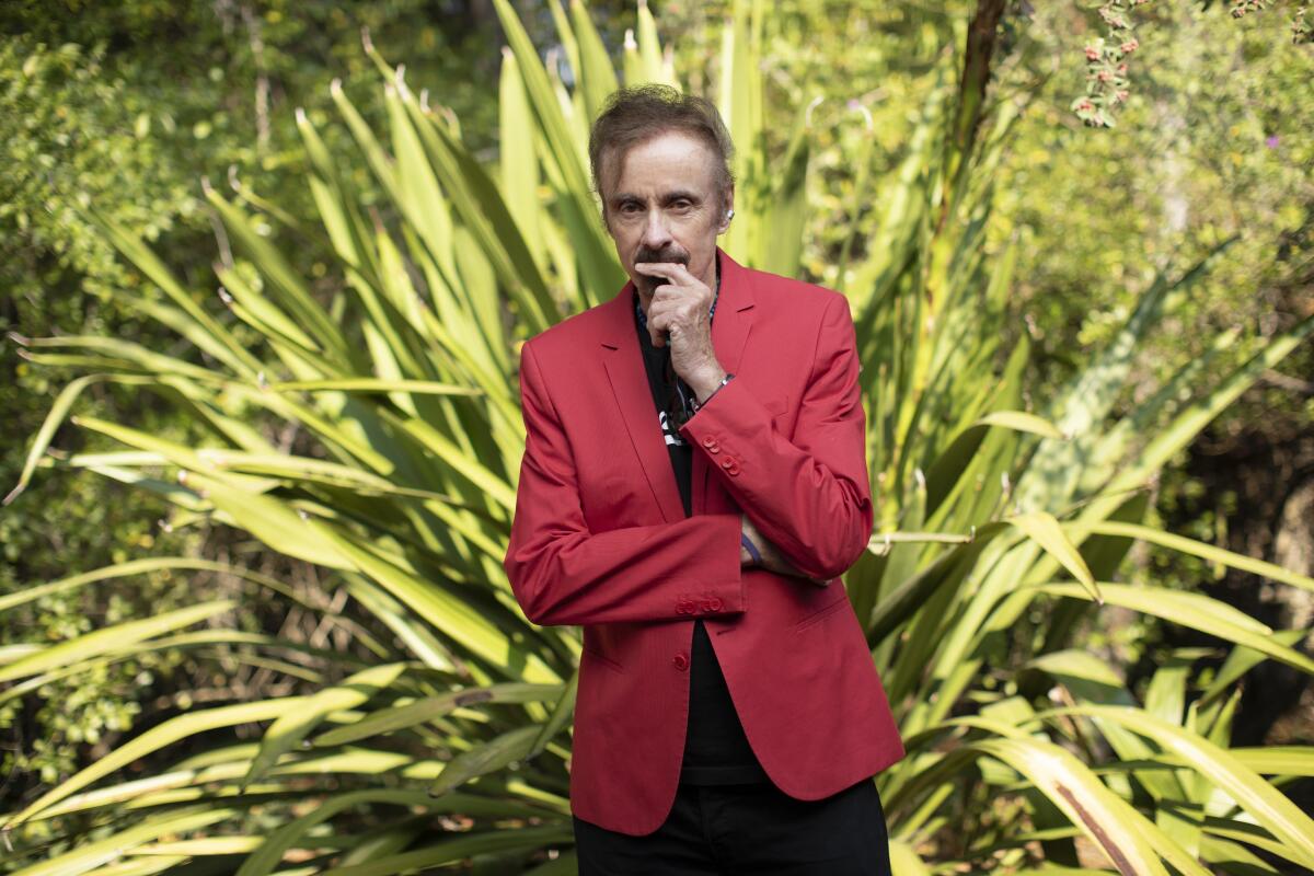 T.C. Boyle, in a red blazer, poses in front of a large plant.