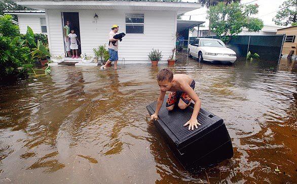 Colby Murphy, age 10, tries to balance on top of a plastic locker while floating in the front yard of Leandro Martinez, center, in Naples, Fla., after Tropical Storm Fay drenched the southwest part of the state.