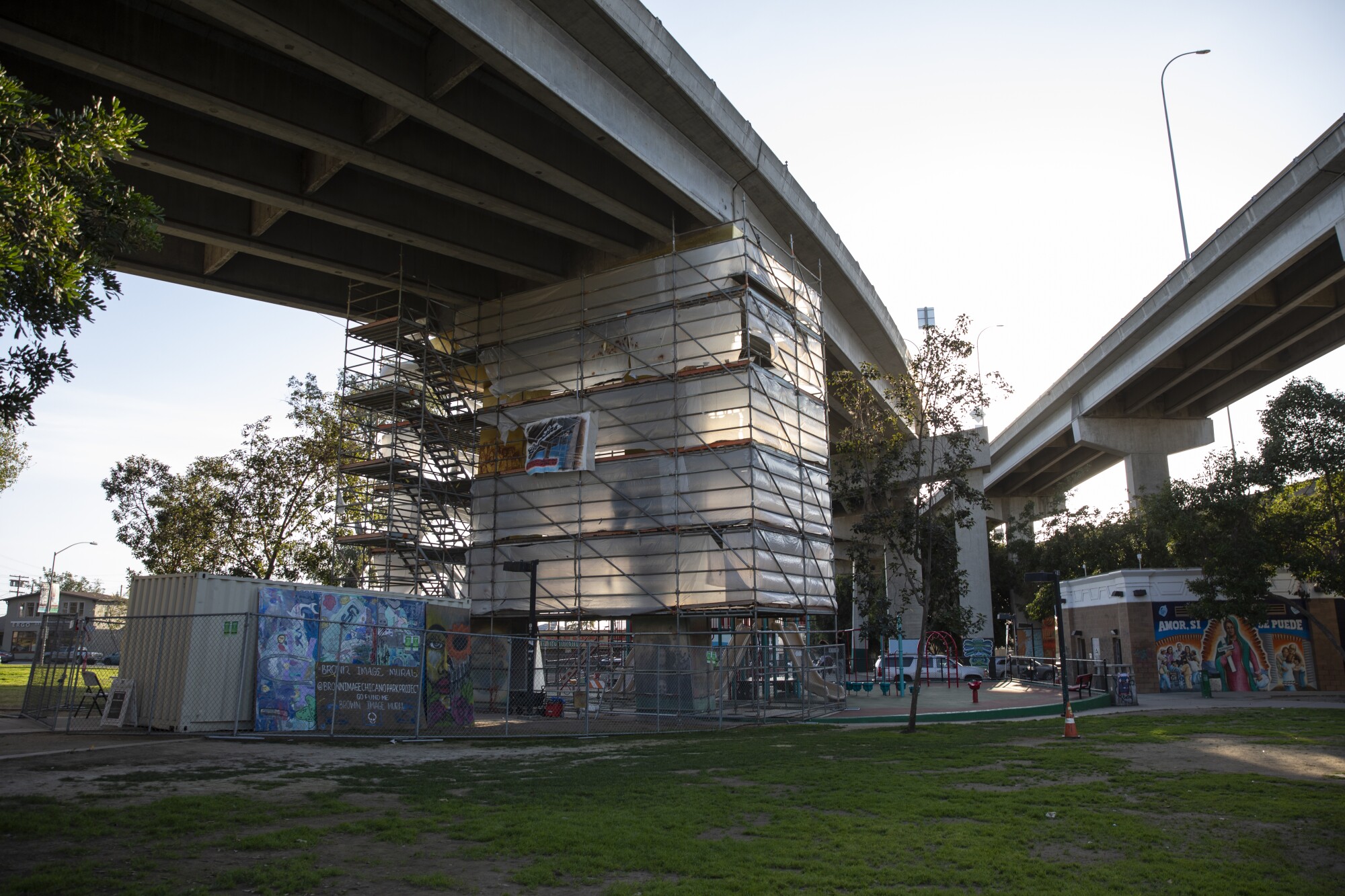 A scaffold surrounds a five-story mural being painted on a pillar in Chicano Park that features images from car clubs.