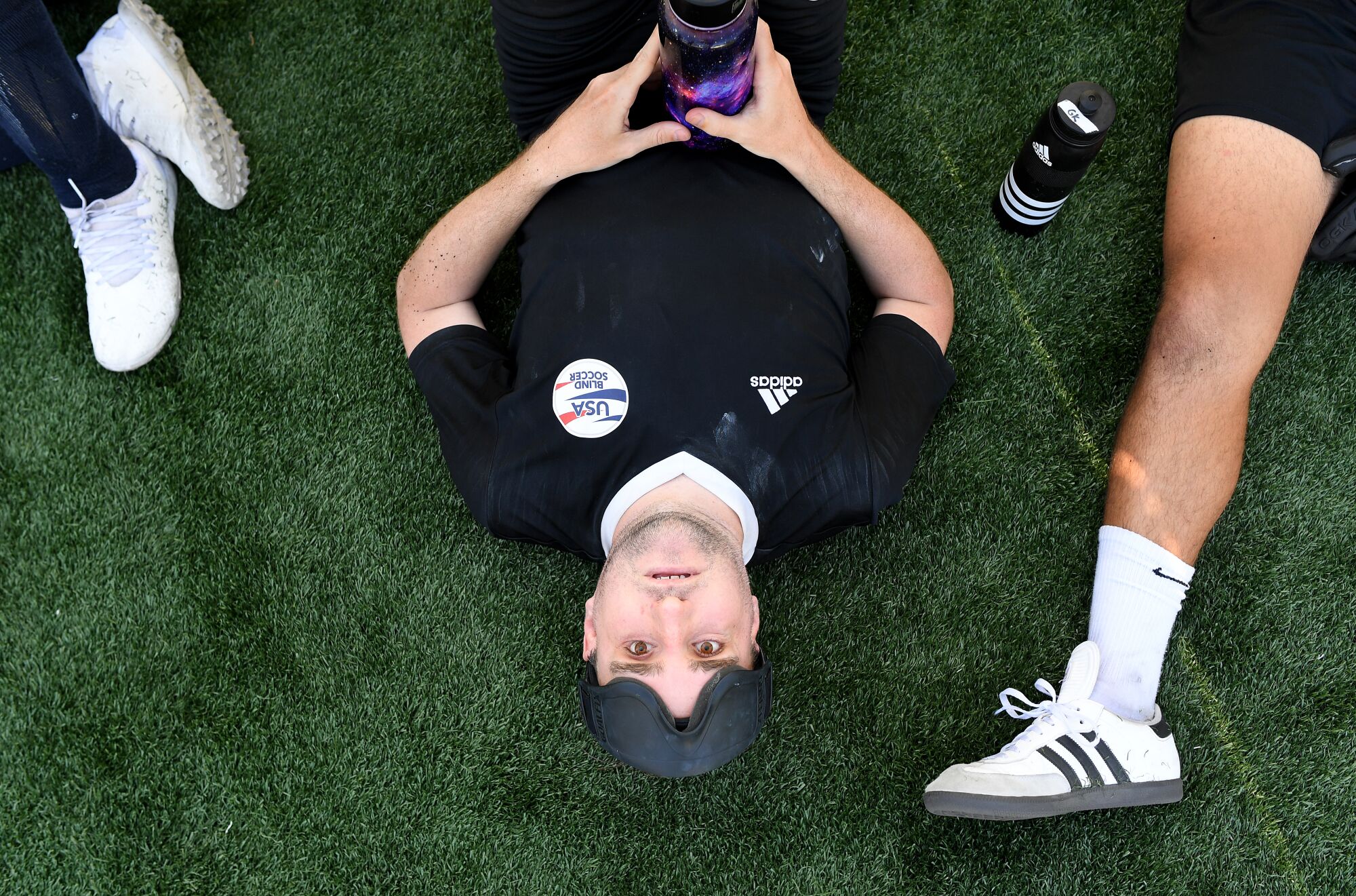 Görme engelli futbolcu Cody Kirchner, gözlüklerini alnına dayayarak sahada yatıyor ve su molası veriyor.