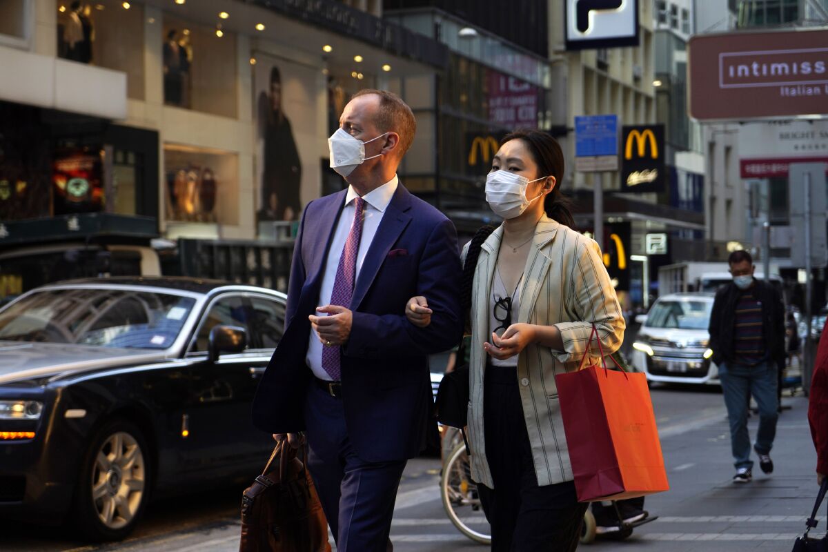 People wearing face masks to protect against the spred of the coronavirus, walk along a street in Hong Kong, Monday, Nov. 30, 2020. (AP Photo/Kin Cheung)
