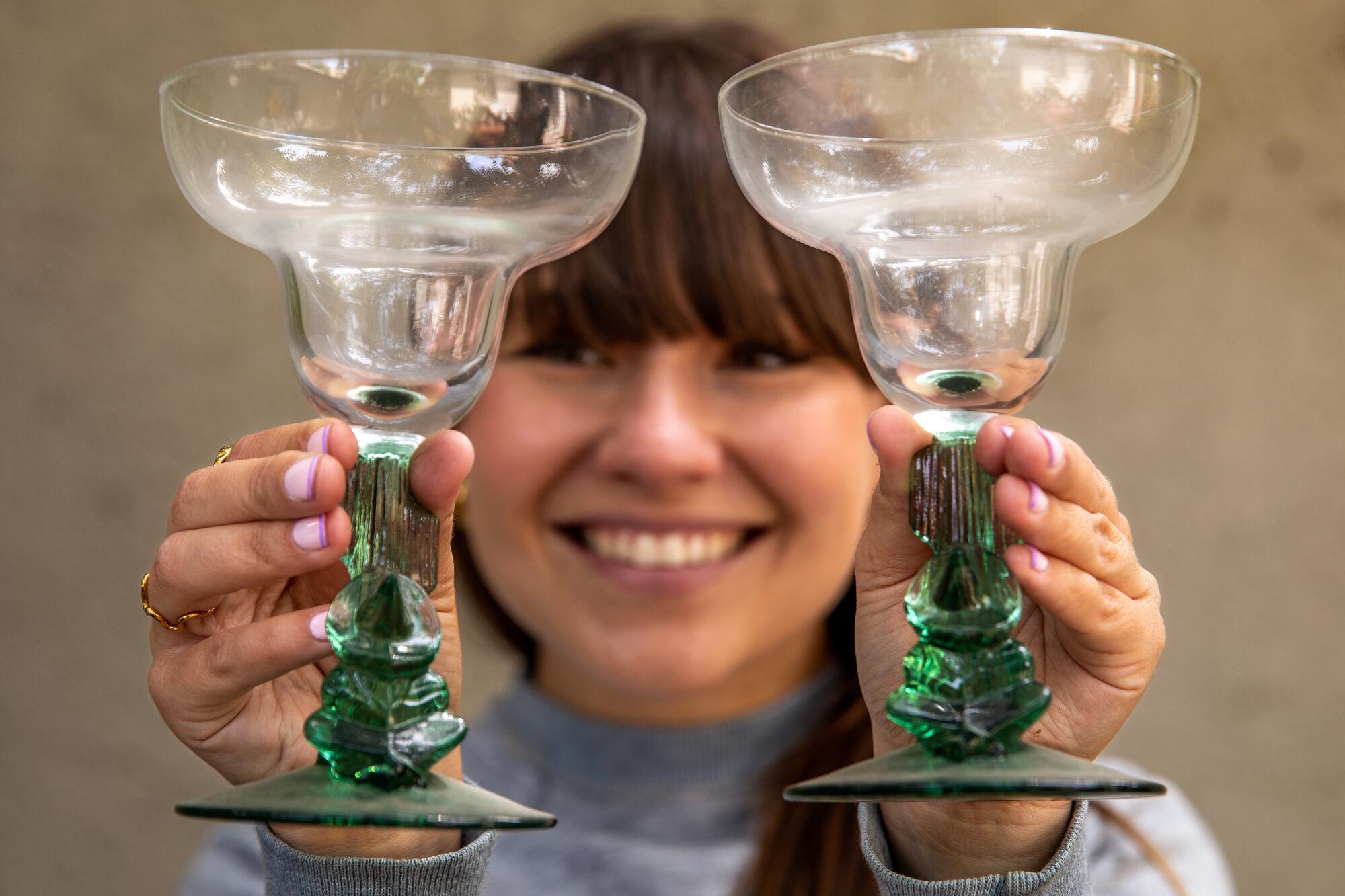 Amy Solomon holds up a pair cocktail glasses with dark green bases.
