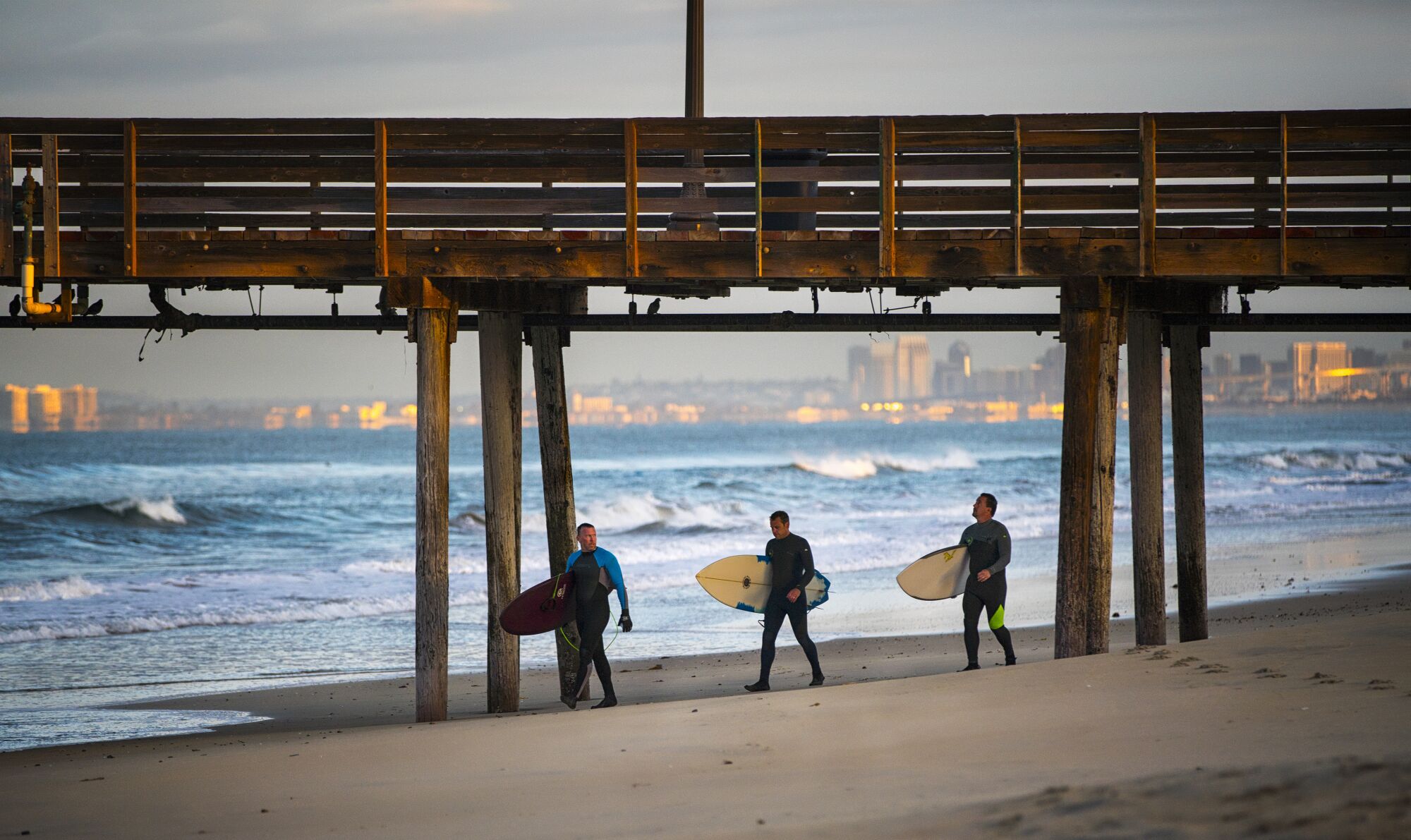 Surfers walk along the beach near Imperial Beach Pier.