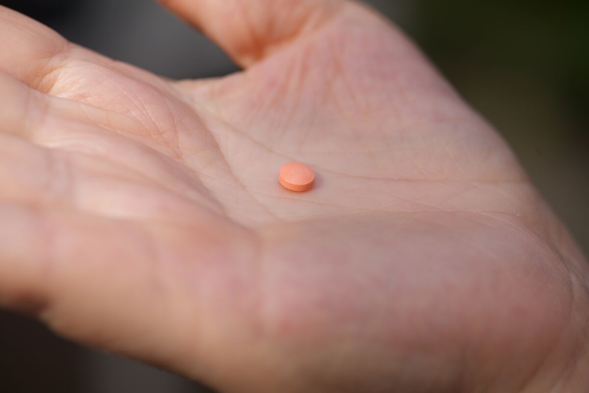 A woman holds an aspirin pill in the palm of her hand.