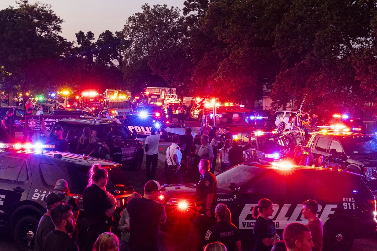 Emergency vehicles flash their lights at 9 p.m. along Lamont Avenue to honor Kalamazoo County Sheriff Deputy Ryan Proxmire outside the Sheriff office in Kalamazoo, Mich., Sunday, Aug. 15, 2021. A deputy in Michigan has died after being wounded during a chase with a gunman. The Kalamazoo County Sheriff’s Office says Deputy Ryan Proxmire died Sunday. Deputies encountered the suspect Saturday evening at a gas station in Galesburg and a chase ensued. (Joel Bissell/Kalamazoo Gazette via AP)