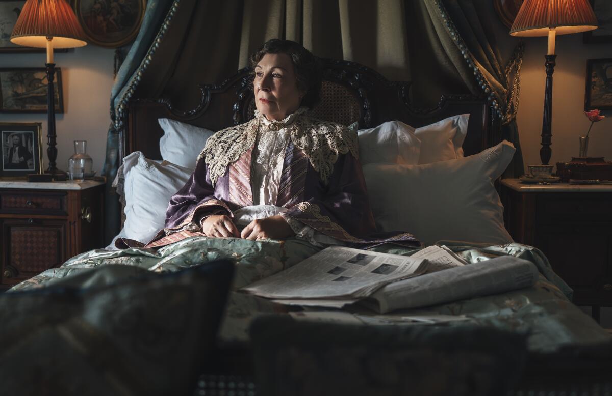 A woman in a dressing gown sits up in bed