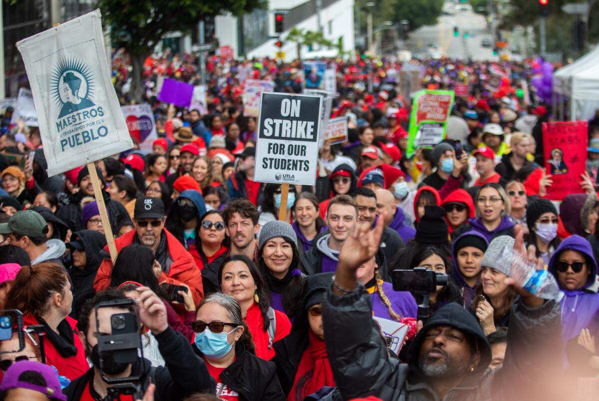 A crowd of protesters; many wearing red and purple. A picket sign says "On Strike For Our Students."