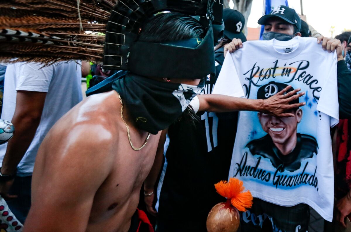 A dancer in an Indigenous headdress touches a shirt reading "Rest in Peace Andres Guardado" at a protest over his killing