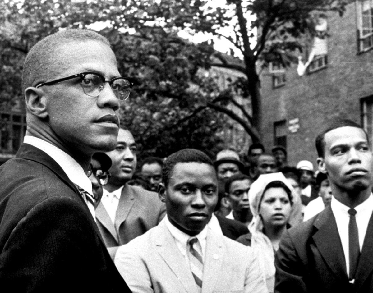 Malcolm X, at a rally, looks off to the side.