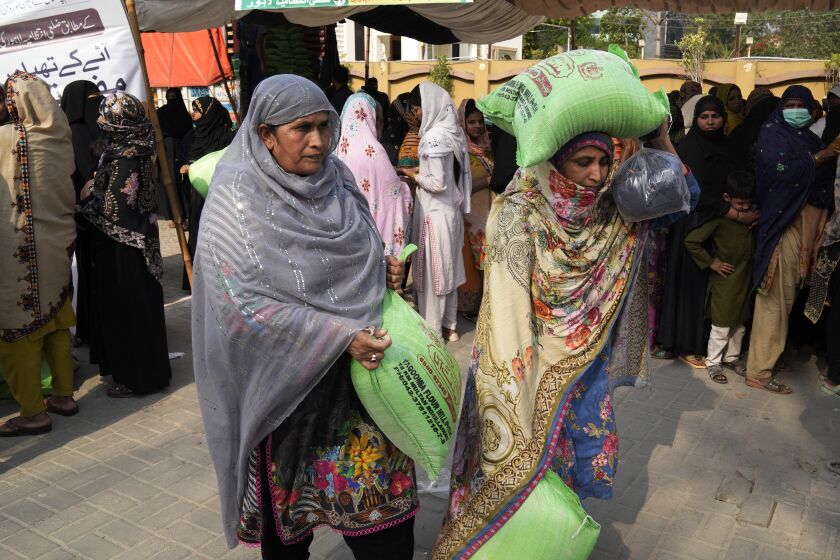 Women leave while others wait their turn to get a free sack of wheat flour at a distribution point, in Lahore, Pakistan, Thursday, March 30, 2023. Government is providing free flour to deserving and poor families during the Muslim's holy month of Ramadan due to high inflation in the country. (AP Photo/K.M. Chaudary)