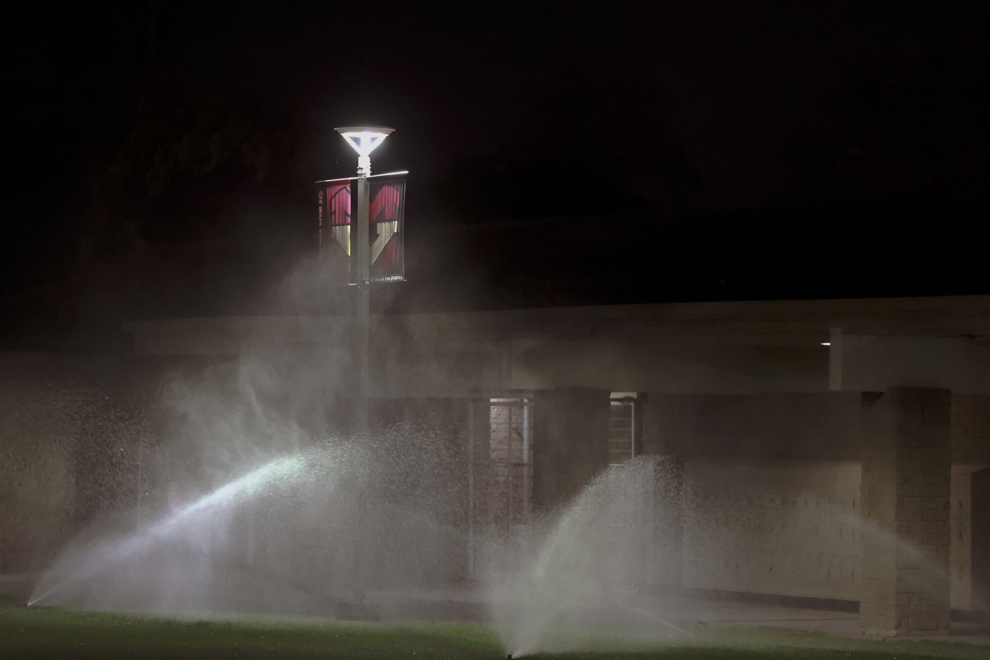 Sprinklers water the grass outside Mission Viejo High School at night