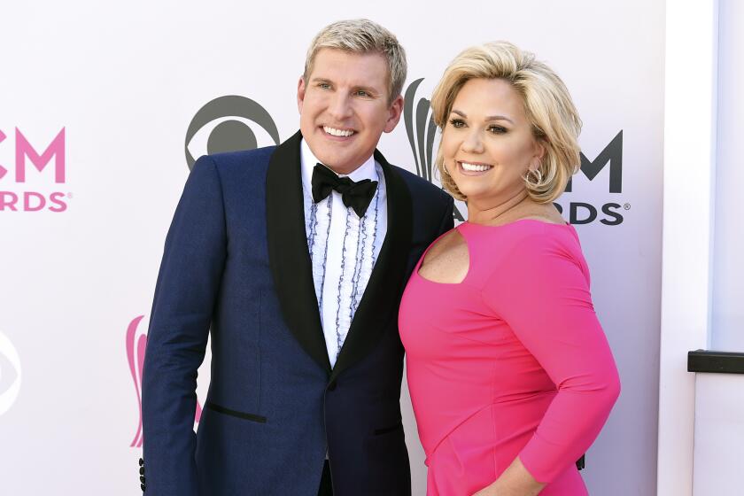 Todd Chrisley in a blue tuxedo and his wife, Julie Chrisley in a pink dress pose for photos