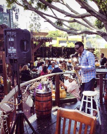 A person plays saxophone to a crowd of diners on an outdoor patio