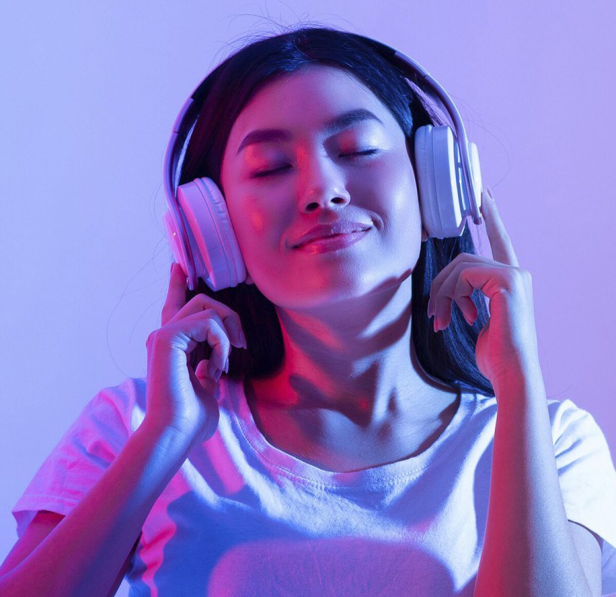 A smiling millennial woman closes her eyes as she listens to music in her headphones. 