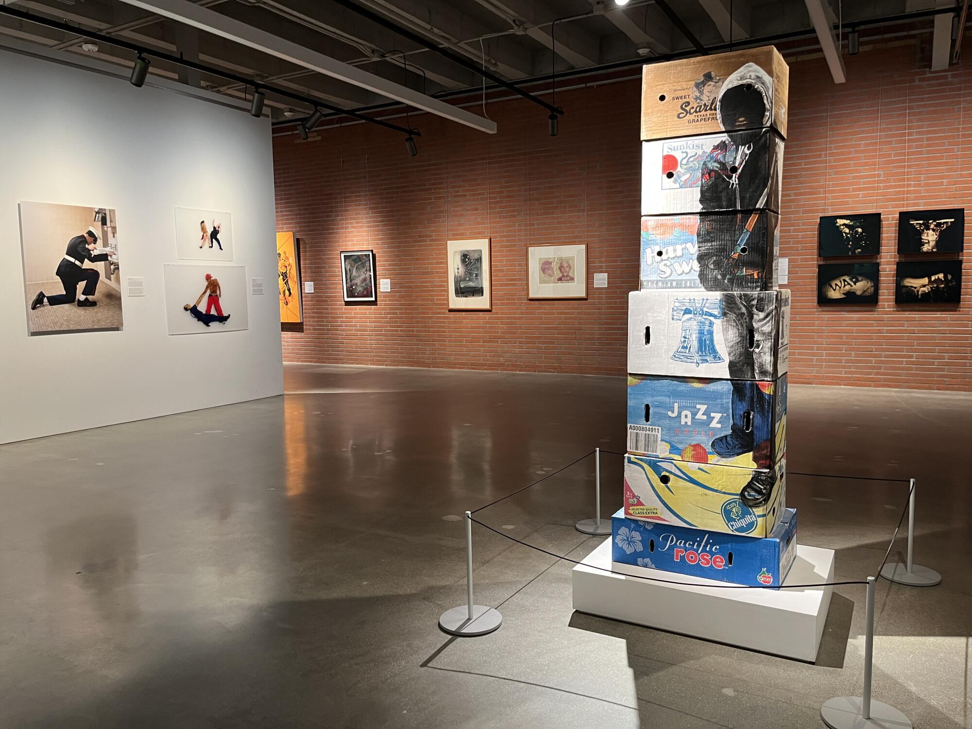 A tower of fruit boxes in a gallery is painted with the figure of a farmworker in a hoodie on the surface.