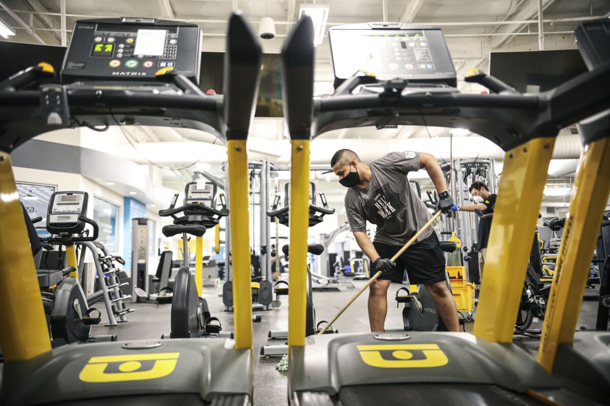 Juan Lopez mops around gym equipment at Chuze Fitness in Chula Vista on Thursday. The gym plans to reopen Saturday.