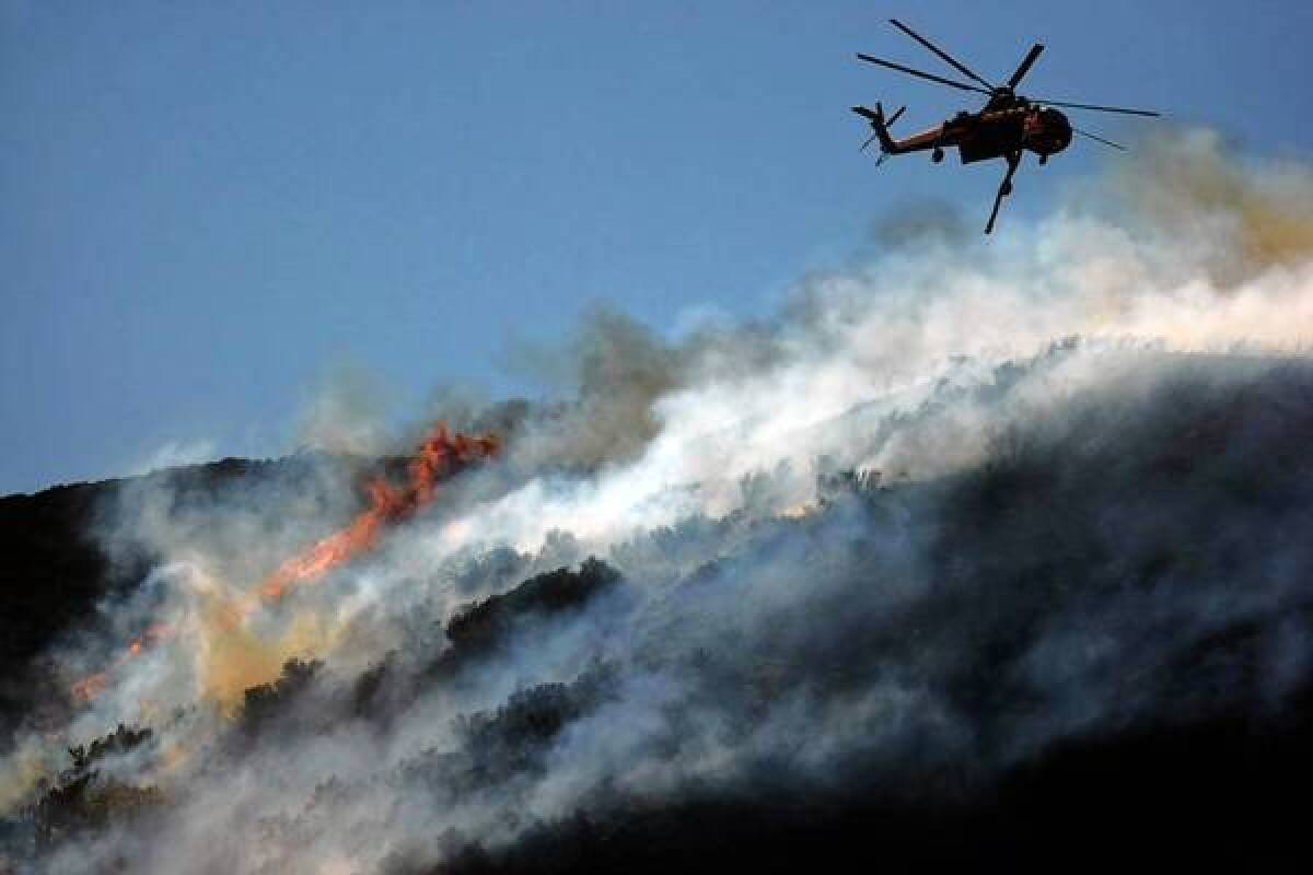 A helicopter drops water on a ridge near Lake Hughes as the Powerhouse fire continues its rampage. The blaze, which started Thursday, has burned more than 32,000 acres and has destroyed at least seven structures.