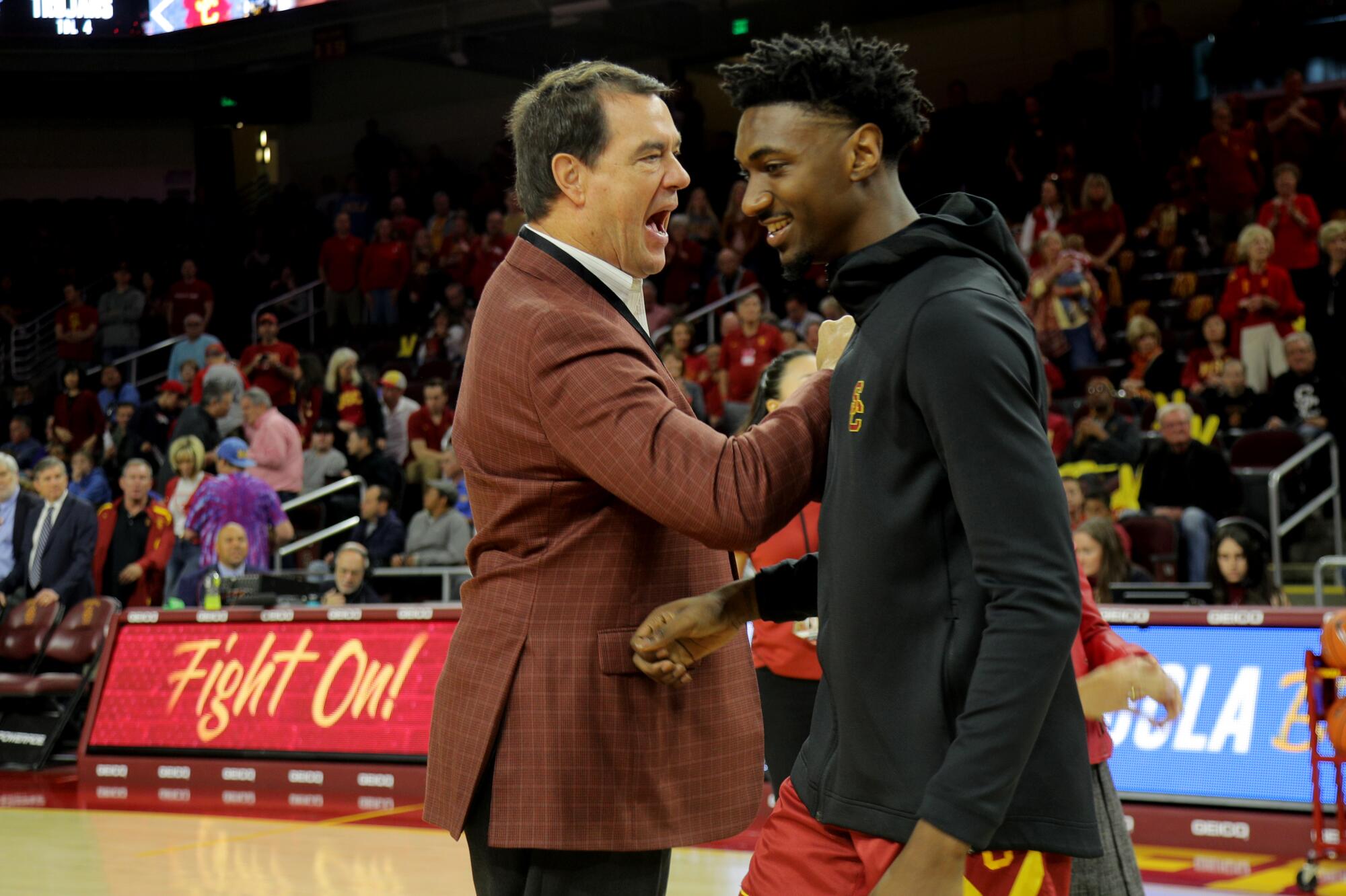 USC athletic director Mike Bohn congratulates guard Jonah Mathews on the basketball court while a crowd look on